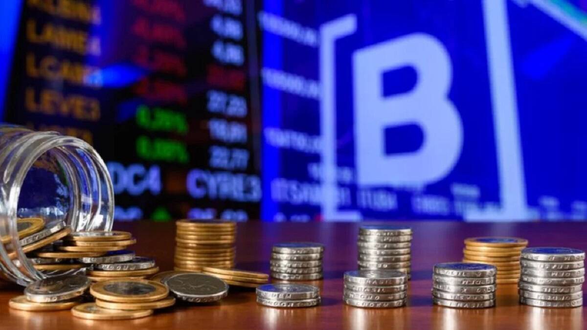 moedas em mesa com painel de ações ao fundo