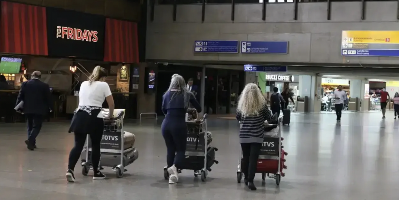 mulheres carregando carrinho de mala em aeroporto